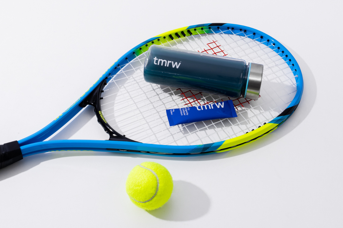 Tmrw drink mix and shaker on a tennis racket with a tennis ball.