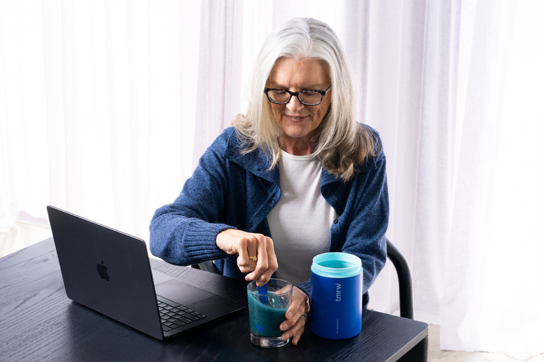  Woman stirring Tmrw supplement drink at desk with laptop.